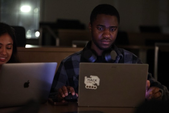 A hacker working on a laptop with a HackUNCP sticker